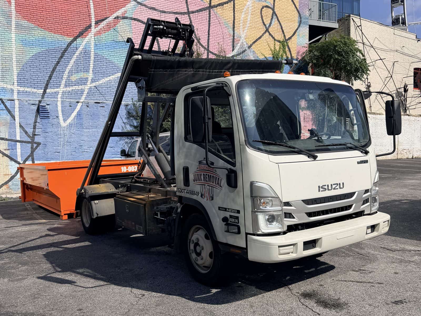 Southside roll-off truck with an orange 10-yard dumpster in a downtown Atlanta lot, mural and Ferris wheel behind