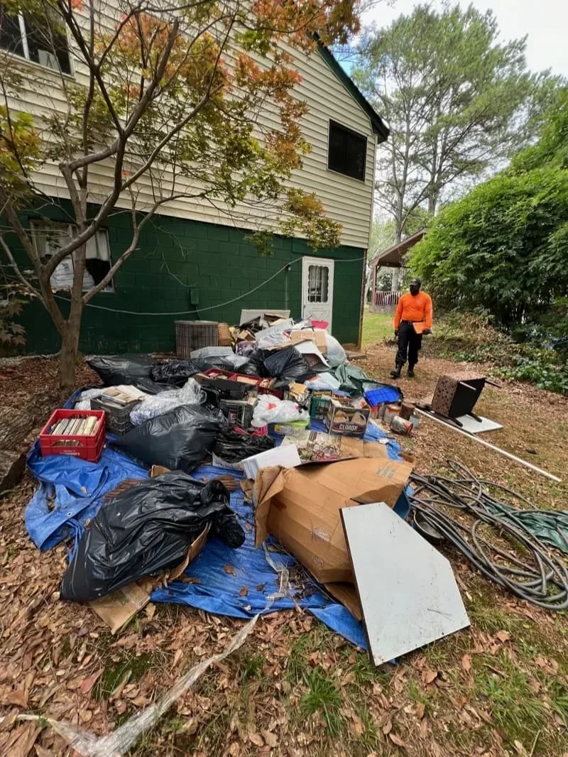 Pile of bagged trash, tarps and debris beside a house before pickup