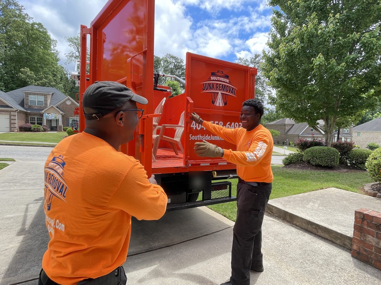 Two Southside crew members loading patio chairs into the back of a junk truck