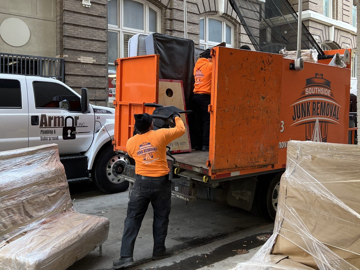 Southside crew loading wrapped furniture into a junk truck outside a commercial building