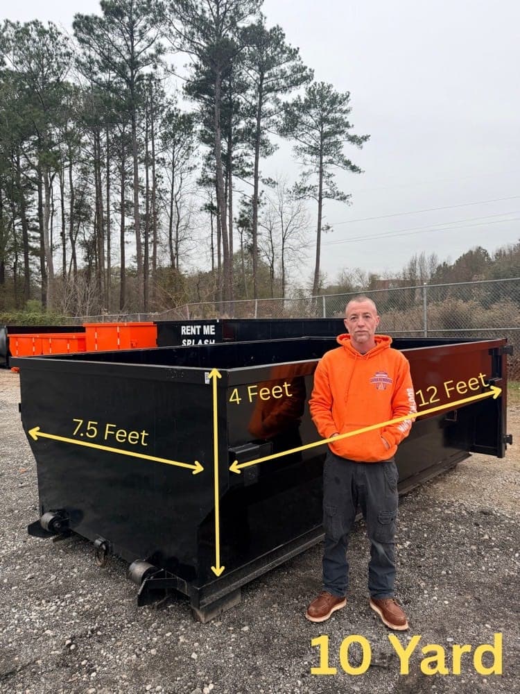 Crew member standing beside the 10-yard orange dumpster with its dimensions marked