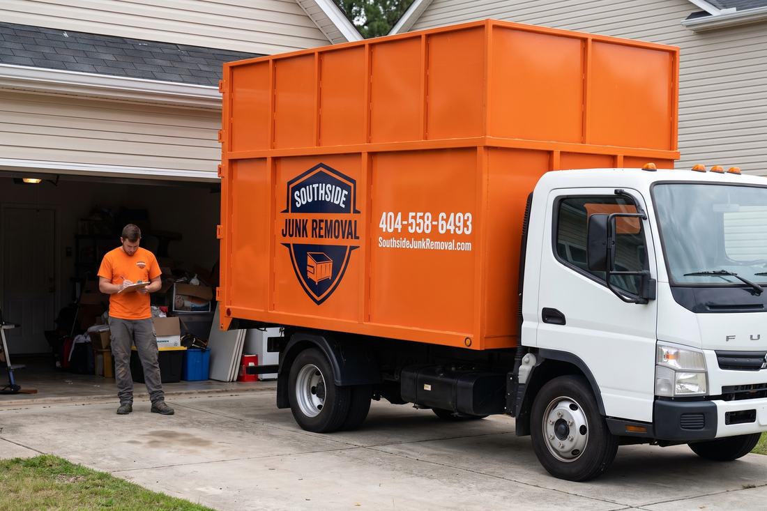 Southside Junk Removal team member writing a free on-site quote on a clipboard at a cluttered garage in McDonough, Georgia, with the orange dump truck on the driveway
