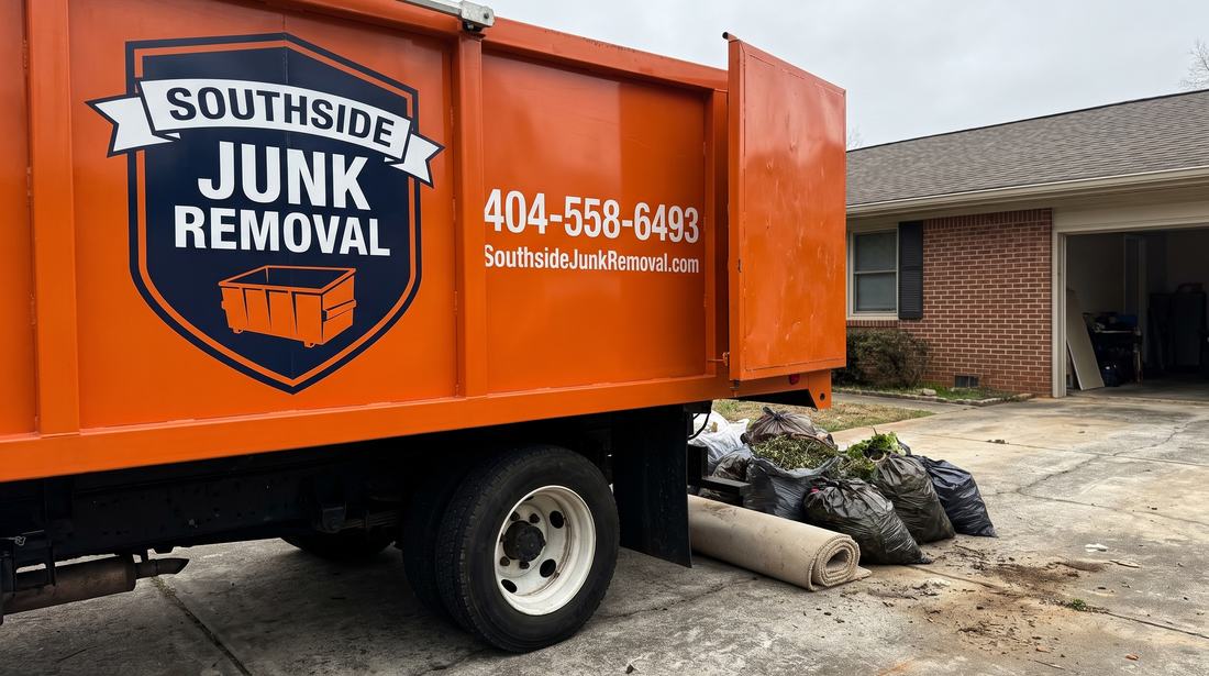 Rear of the orange Southside Junk Removal dump truck backed onto a driveway in Ellenwood, Georgia, with bagged yard waste and rolled carpet waiting to load