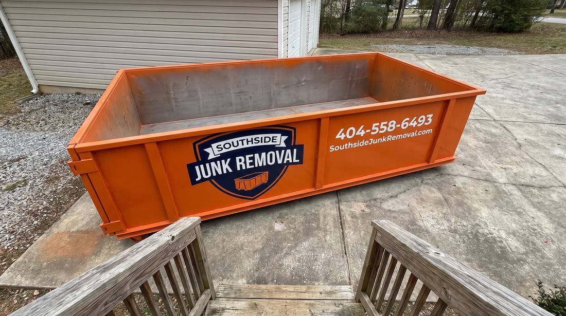 Empty orange Southside Junk Removal roll-off dumpster on a driveway beside a garage in Fairburn, Georgia